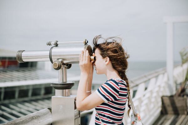 Goal Setting: Girl on boardwalk looking through a telescope, looking to the horizon.